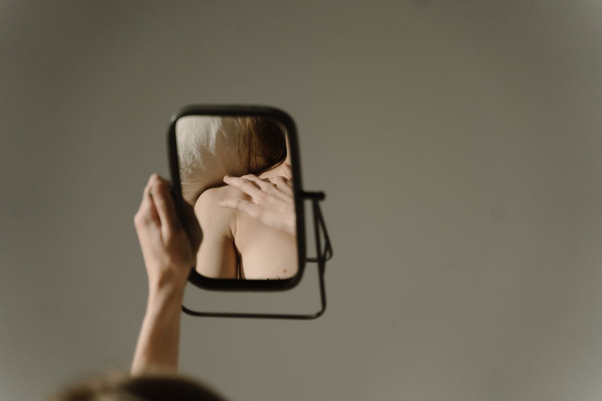 Artistic close-up of thoughtful woman studying her reflection aligning with optics questions about mirrored perception