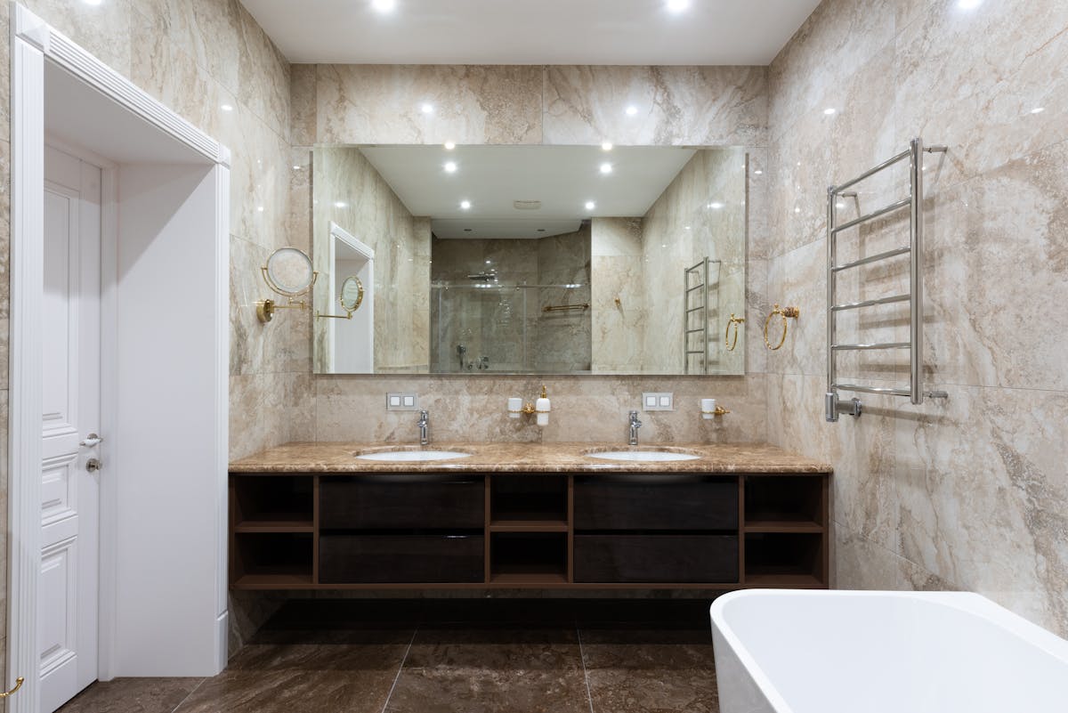 Hands adjusting a framed wall mirror over a sink in a small bathroom