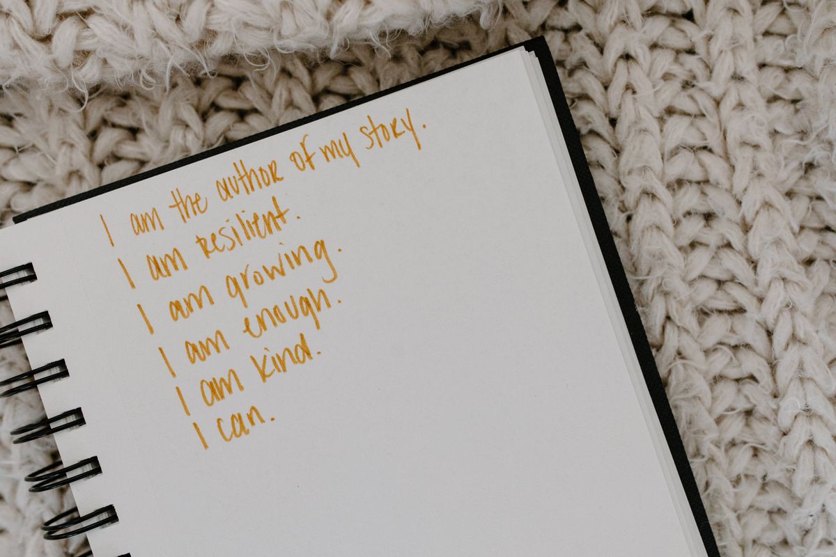 A notebook open to a page filled with handwritten affirmations and personal growth statements on a knitted fabric surface