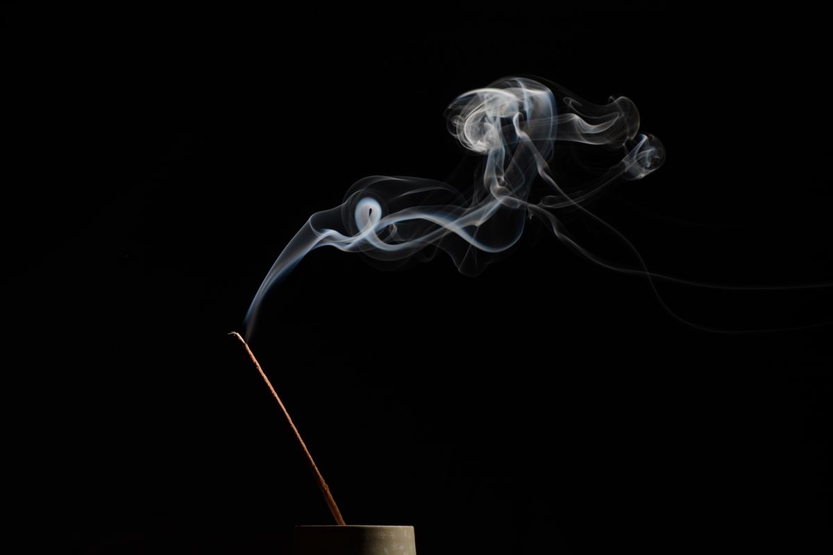 Incense stick releasing soft smoke in soft warm light for home cleansing ritual atmosphere
