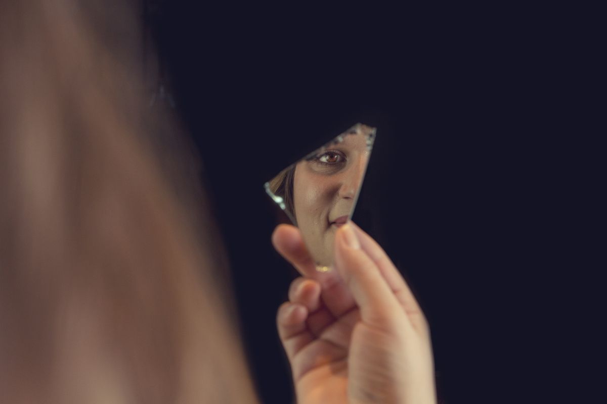 A person's eye and face reflected in a shard of a broken mirror against a dark background representing psychological fracture and identity crisis in cinema