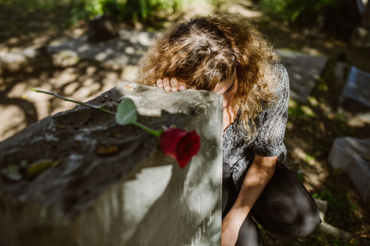 A woman kneeling in grief at a graveside in a cemetery representing the experience of dreaming about deceased loved ones appearing in mirror reflections