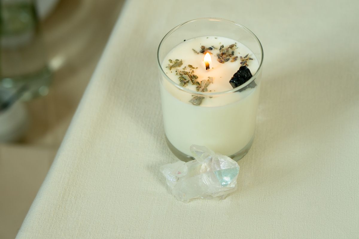 Lit aromatherapy candle surrounded by crystals and herbs representing the need for grounding and safety when engaging in spiritual mirror work