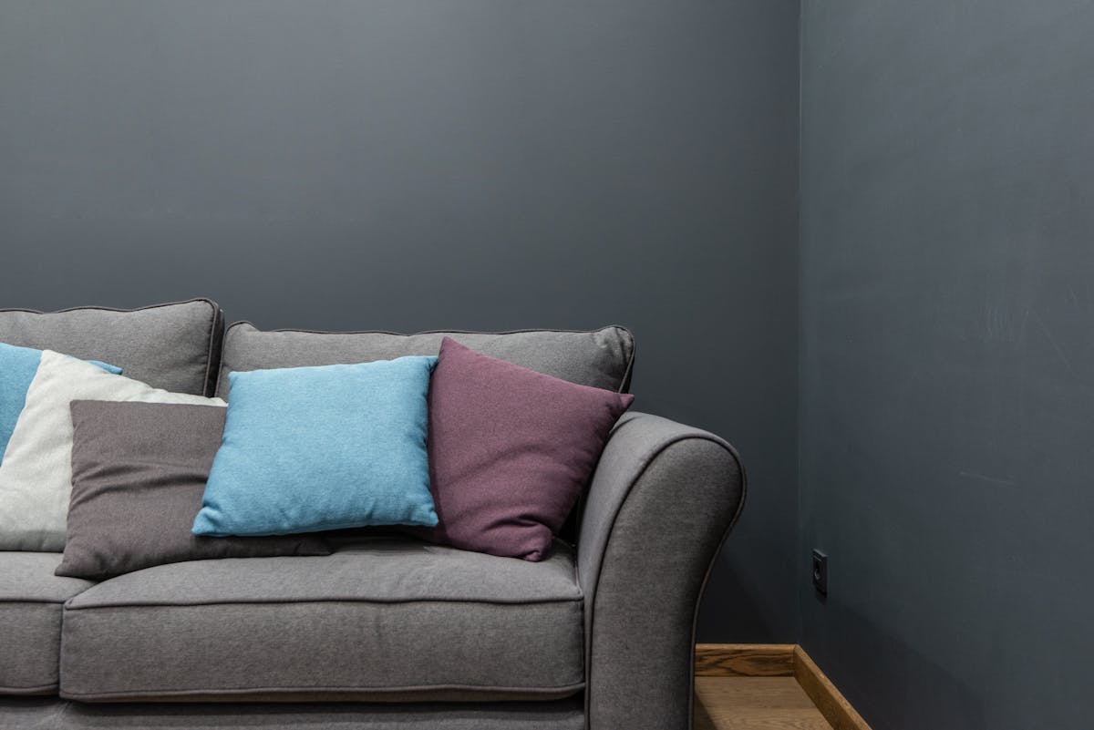 Sofa against a solid wall illustrating the most important feng shui sofa placement rule Grey sofa with cushions placed against a wall in a bright living room, illustrating the main feng shui sofa placement rule