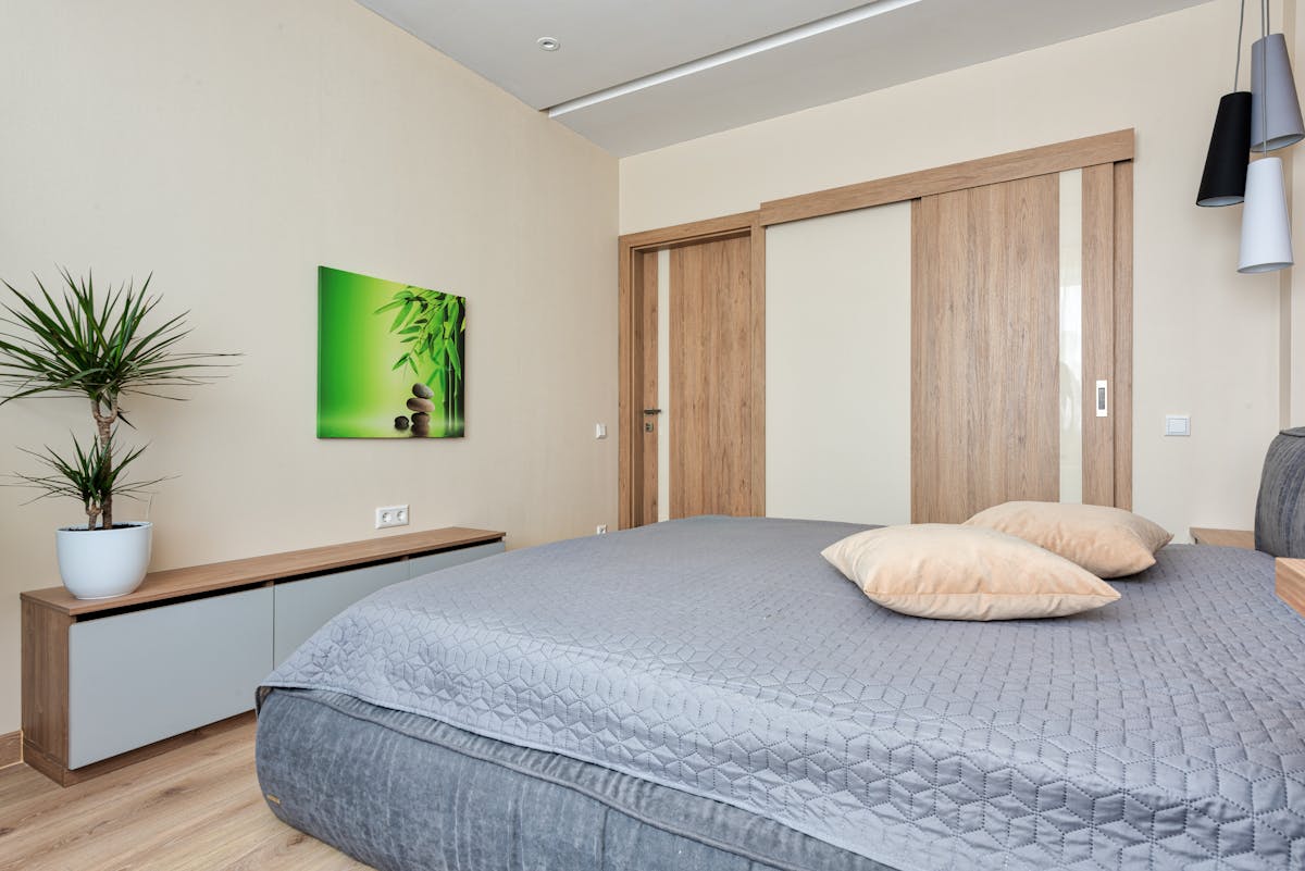 Sliding wardrobe doors in a contemporary bedroom as a sliding wardrobe mirror option Contemporary bedroom with wooden sliding wardrobe doors beside a potted plant showing a sliding wardrobe mirror door option