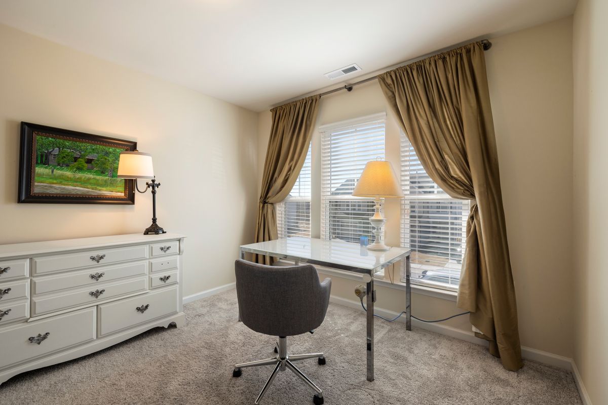 Home office desk beside a window illustrating a feng shui office layout with a window Cozy home office with a glass desk and upholstered chair beside a window, illustrating a feng shui office layout with a window