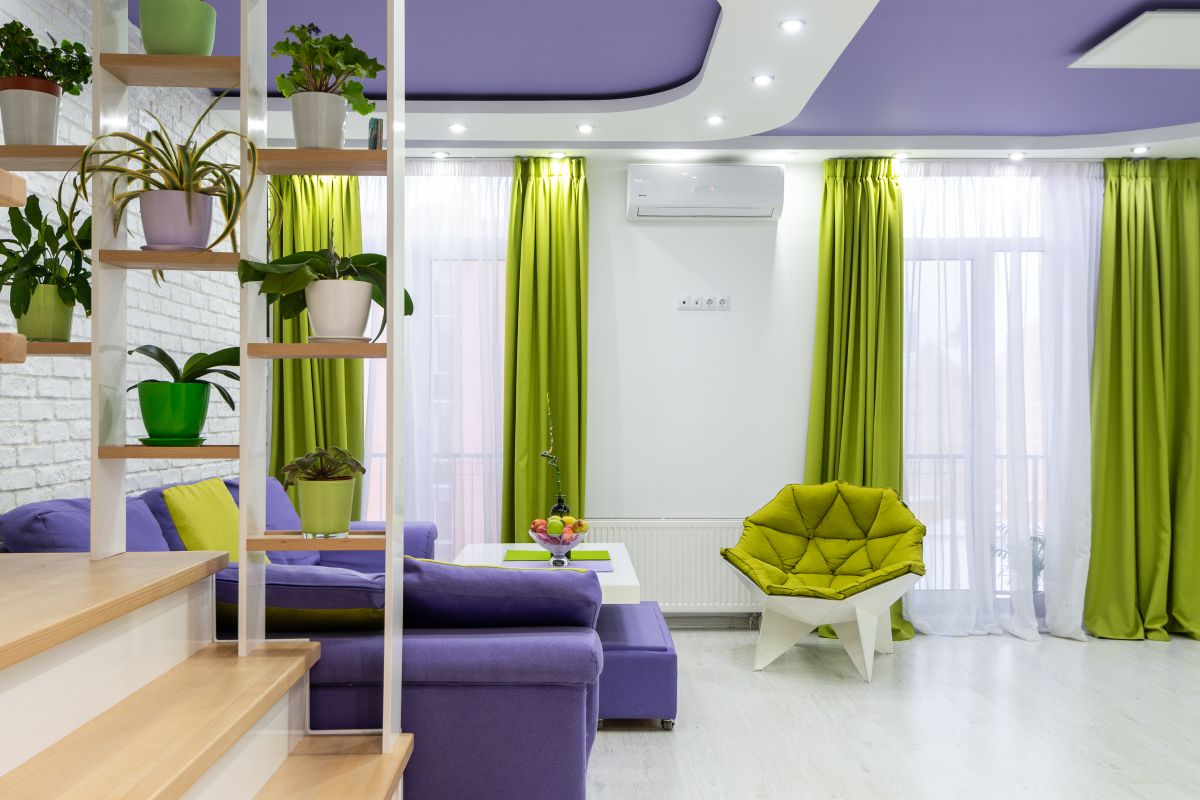 Bright living room with a purple sofa, green armchair and plants, illustrating feng shui prosperity colors