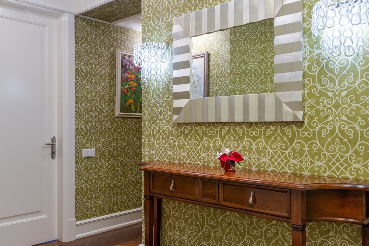 Sophisticated hallway with ornate wallpaper, a wooden console, and a mirror at eye level