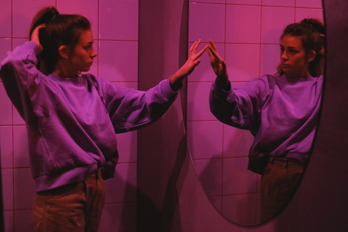 Pink-lit interior portrait studying reflection illustrating contemplative closure after exploring mirror portal symbolism