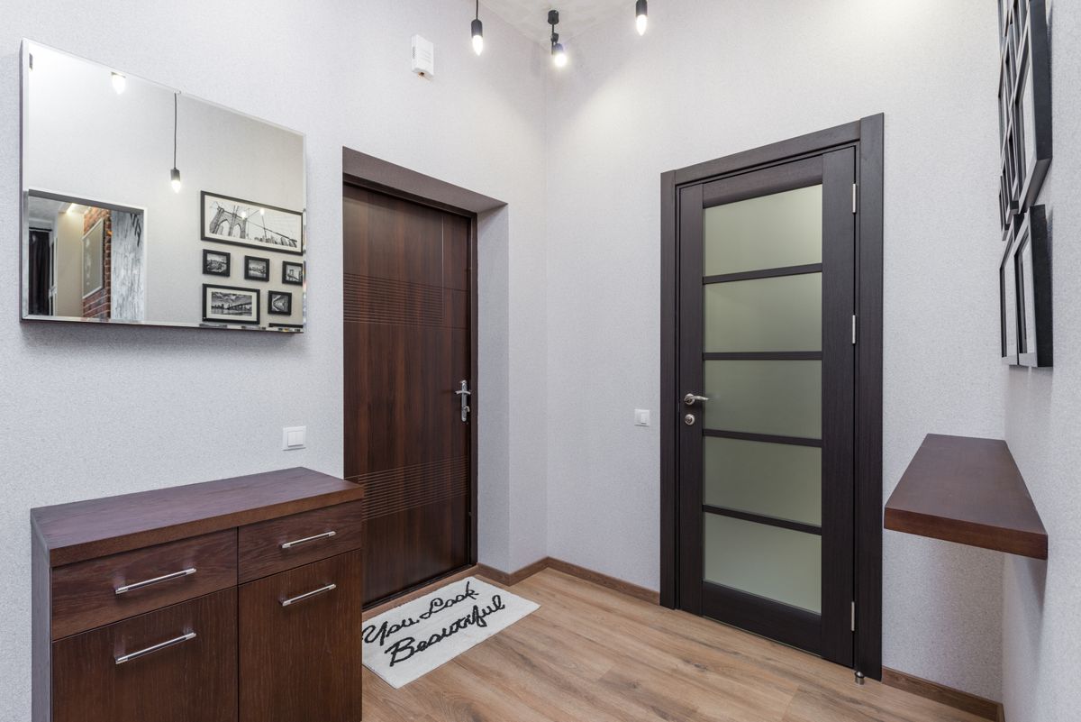 Dark wood-framed mirror in an entryway illustrating wood types for mirror frames Stylish entryway with dark wood elements, a wood-framed mirror, and framed art, illustrating wood types for mirror frames