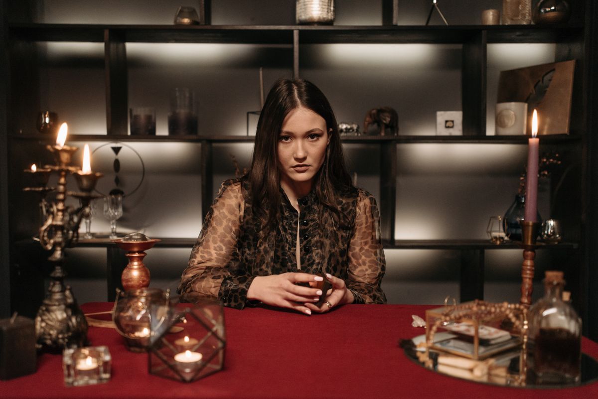 Mysterious woman in a dimly lit room engaged in fortune telling with candles and tarot cards creating a spiritual atmosphere