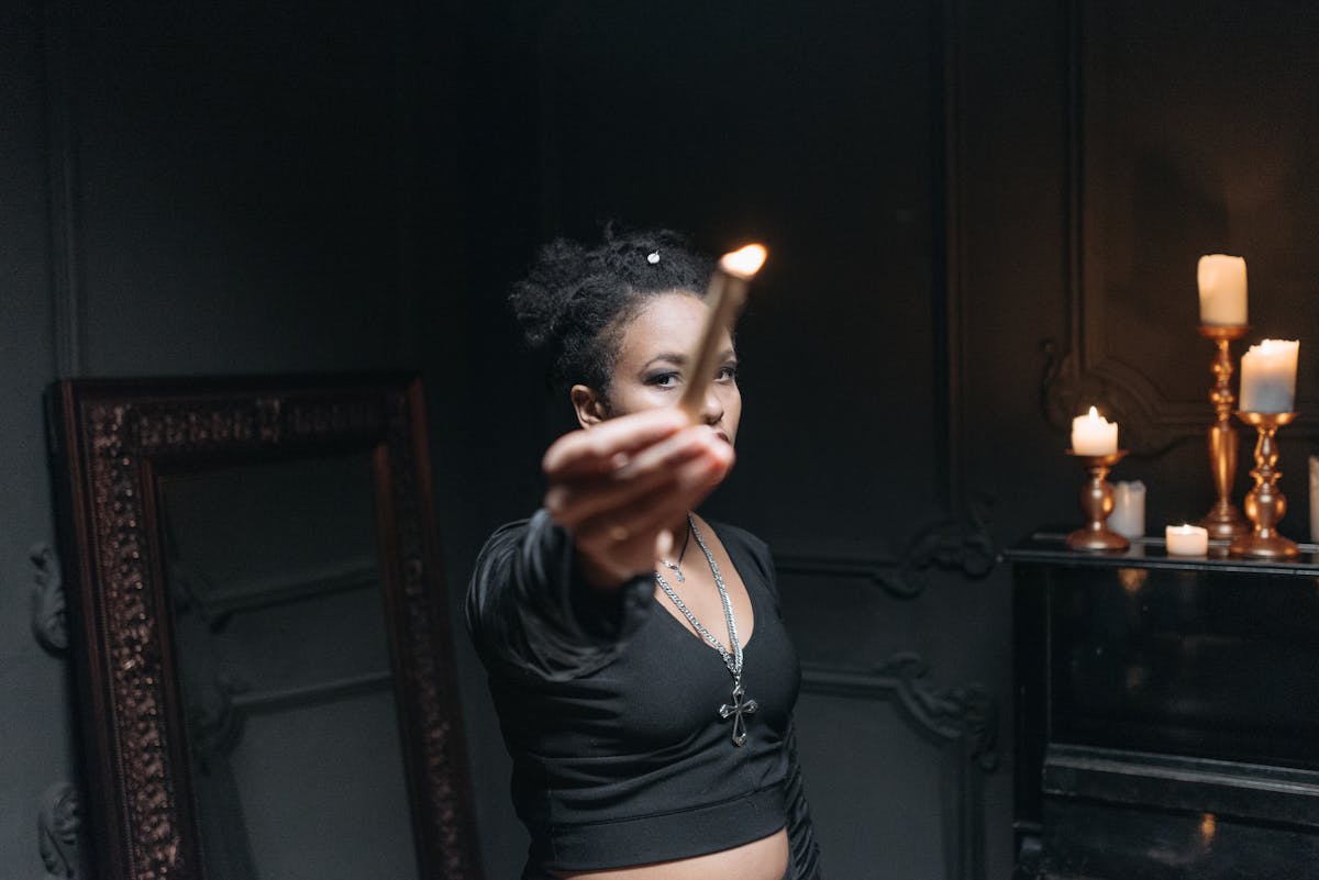 Person holding a single burning candle in a dark room setting up for a black mirror scrying ritual