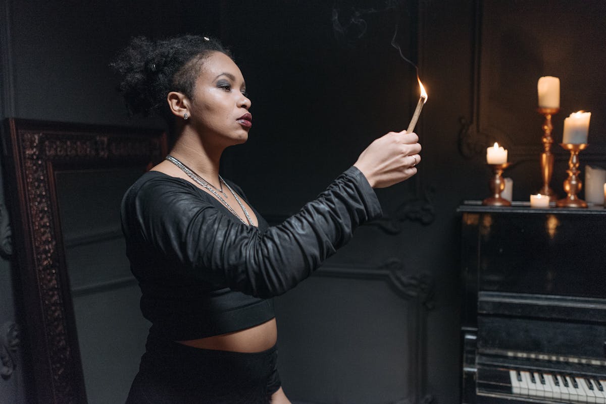 Person holding a burning sage bundle to cleanse a ritual object representing the cleansing step before black mirror scrying