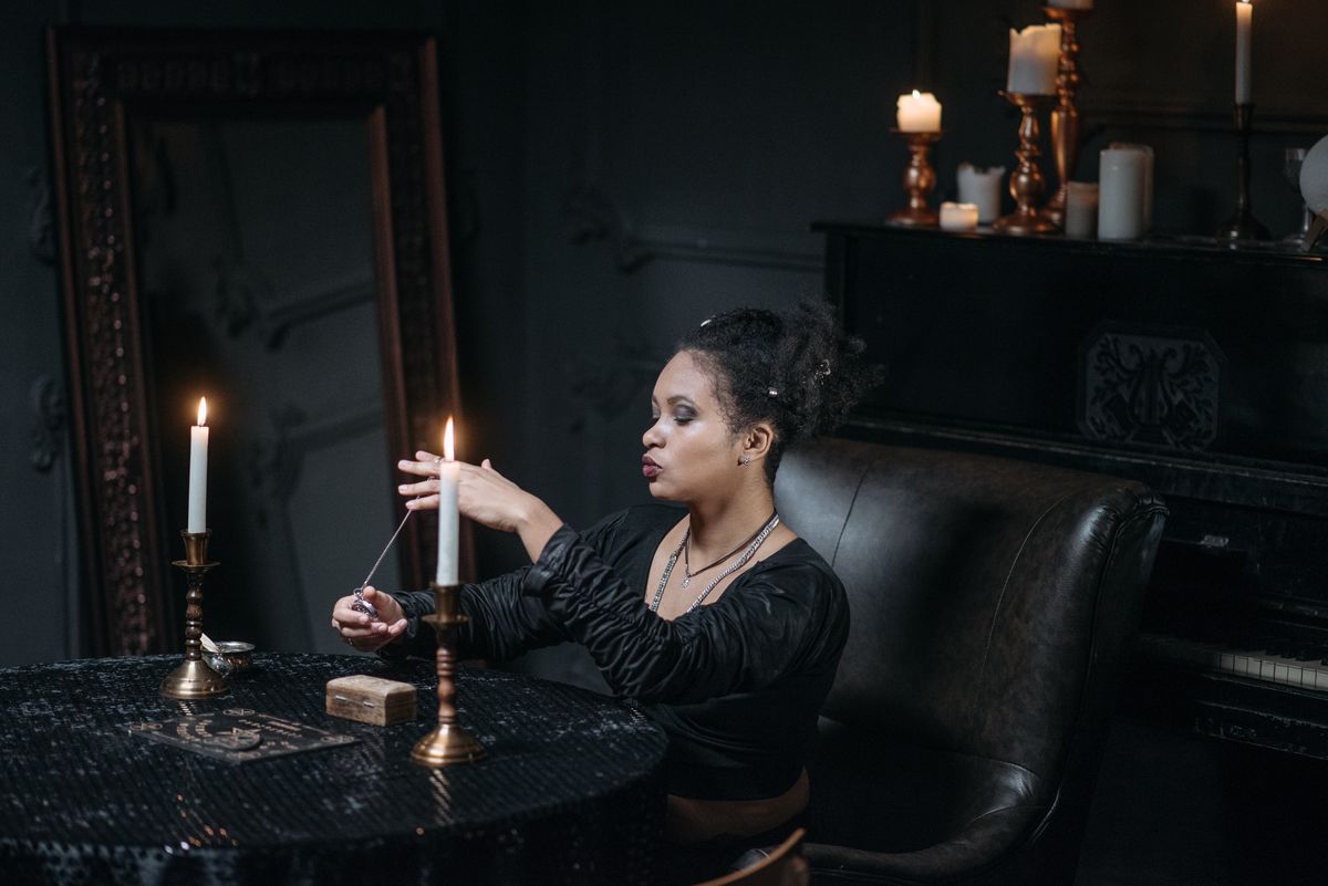 Person meditating with a pendulum in candlelight during a focused black mirror scrying divination session