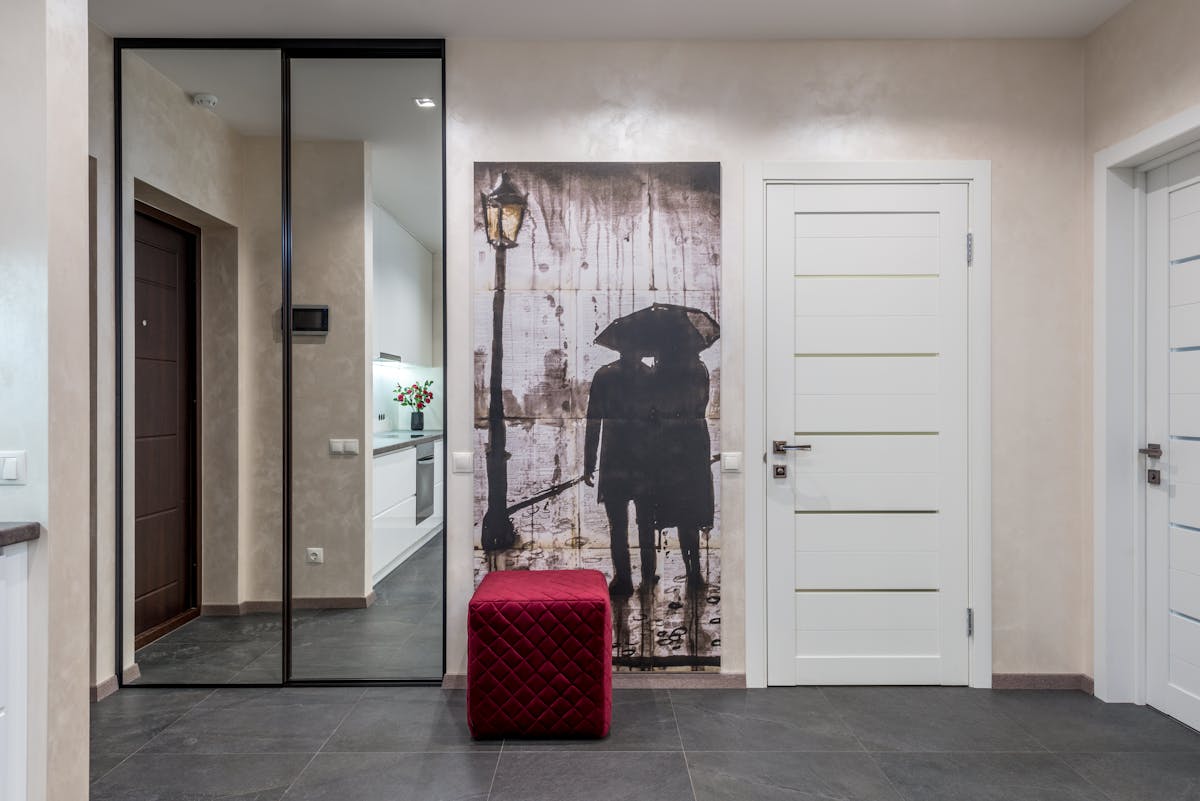 Mirrored wardrobe doors reflecting a bright room, illustrating the benefits of a mirror for a wardrobe Wardrobe with mirrored doors and a red pouf in a bright room showing how a mirror for a wardrobe reflects light