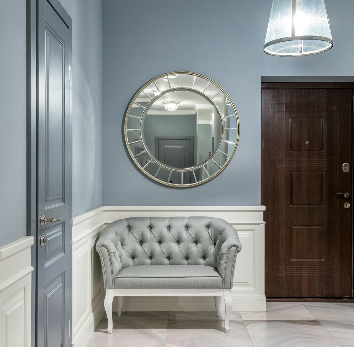 A modern and stylish hallway with a round mirror and tufted armchair, offering a welcoming ambience