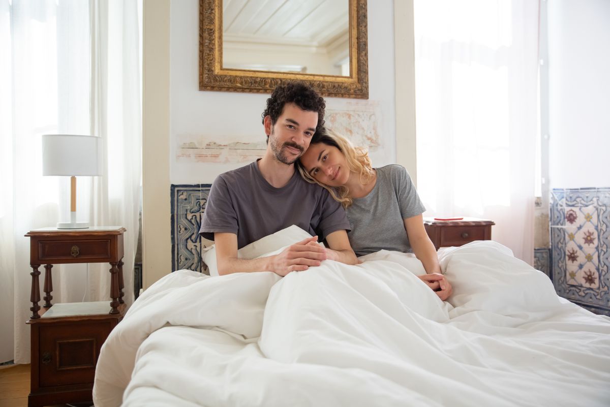 Happy couple relaxing together in a bright, cozy bedroom, illustrating shared feng shui sleeping direction decisions