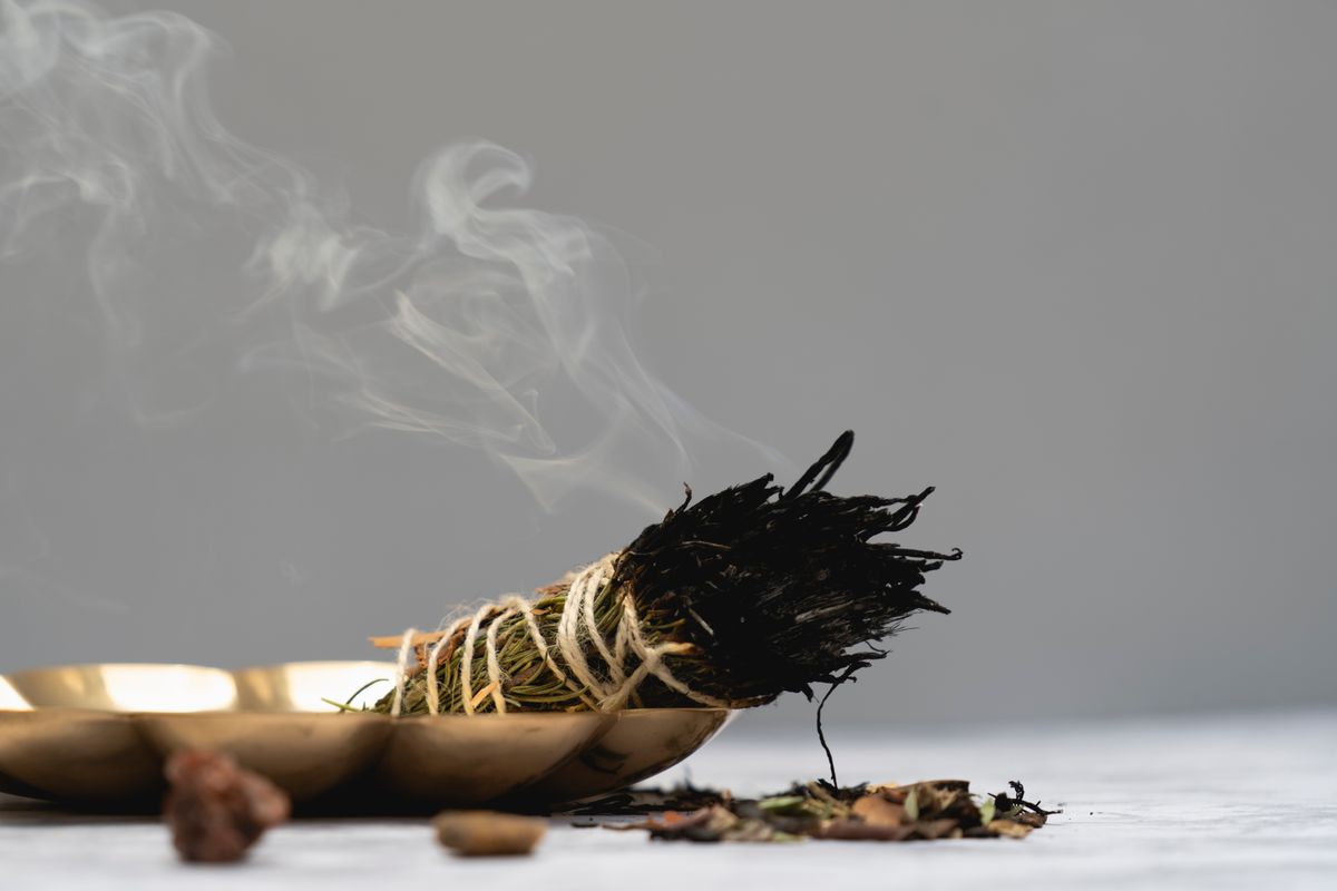 Calm spiritual atmosphere with a herbal sage smudge burning on a wooden table representing the purification step in the broken mirror spiritual meaning