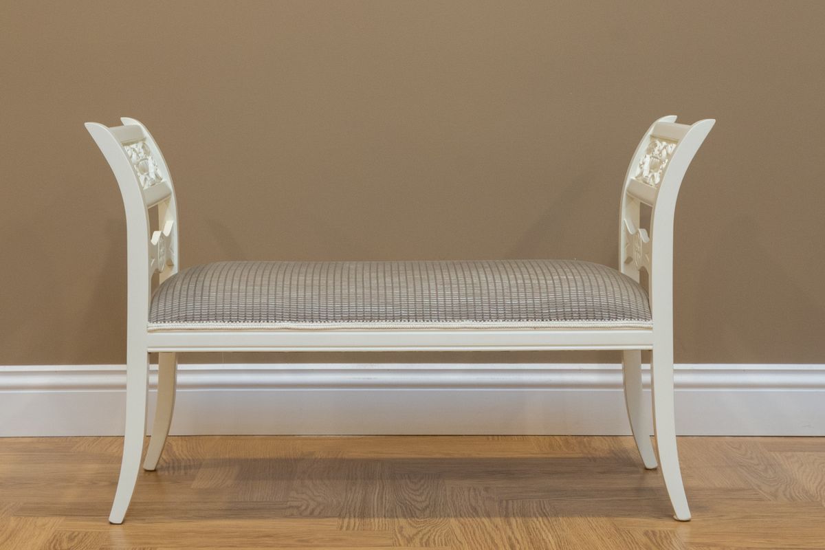 White entryway bench illustrating how to size and place a mirror above it Classic white wooden bench against a beige wall, showing how to size a mirror above an entryway bench