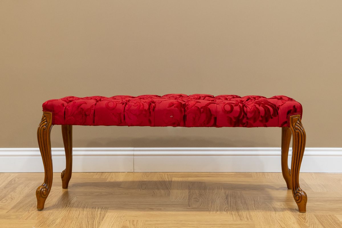 Upholstered bench illustrating a stylish entryway bench with mirror combo Luxurious red upholstered bench with wooden legs against a beige wall, showing a stylish entryway bench with mirror combo