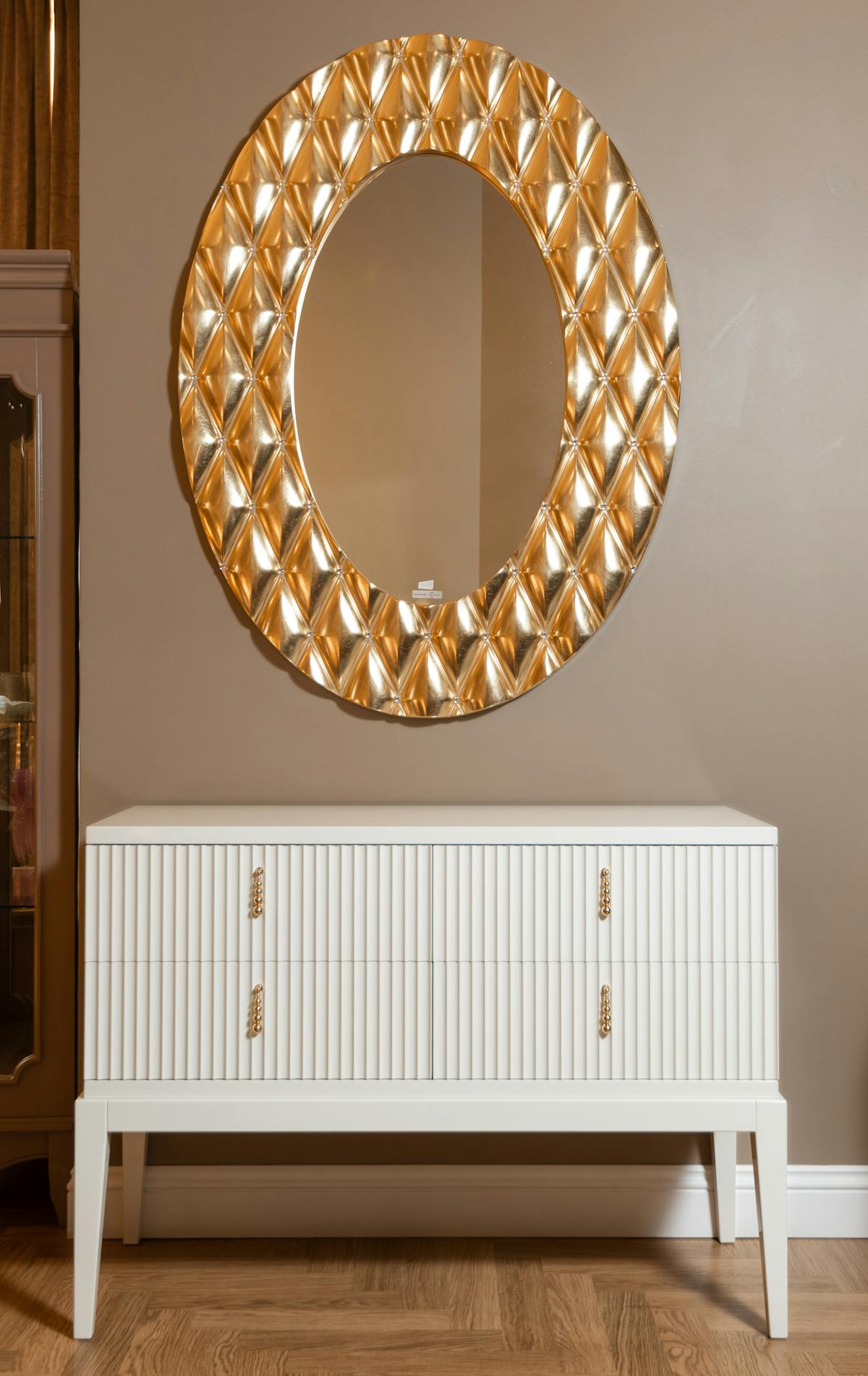 Elegant gold ornate mirror above a white cabinet in a styled neutral interior
