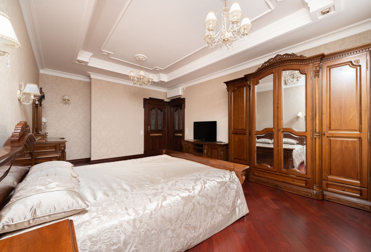 Rich wood finishes in a luxurious bedroom illustrating wood mirror frame finish options Luxurious bedroom with rich wooden furniture and chandelier lighting, illustrating wood mirror frame finishes