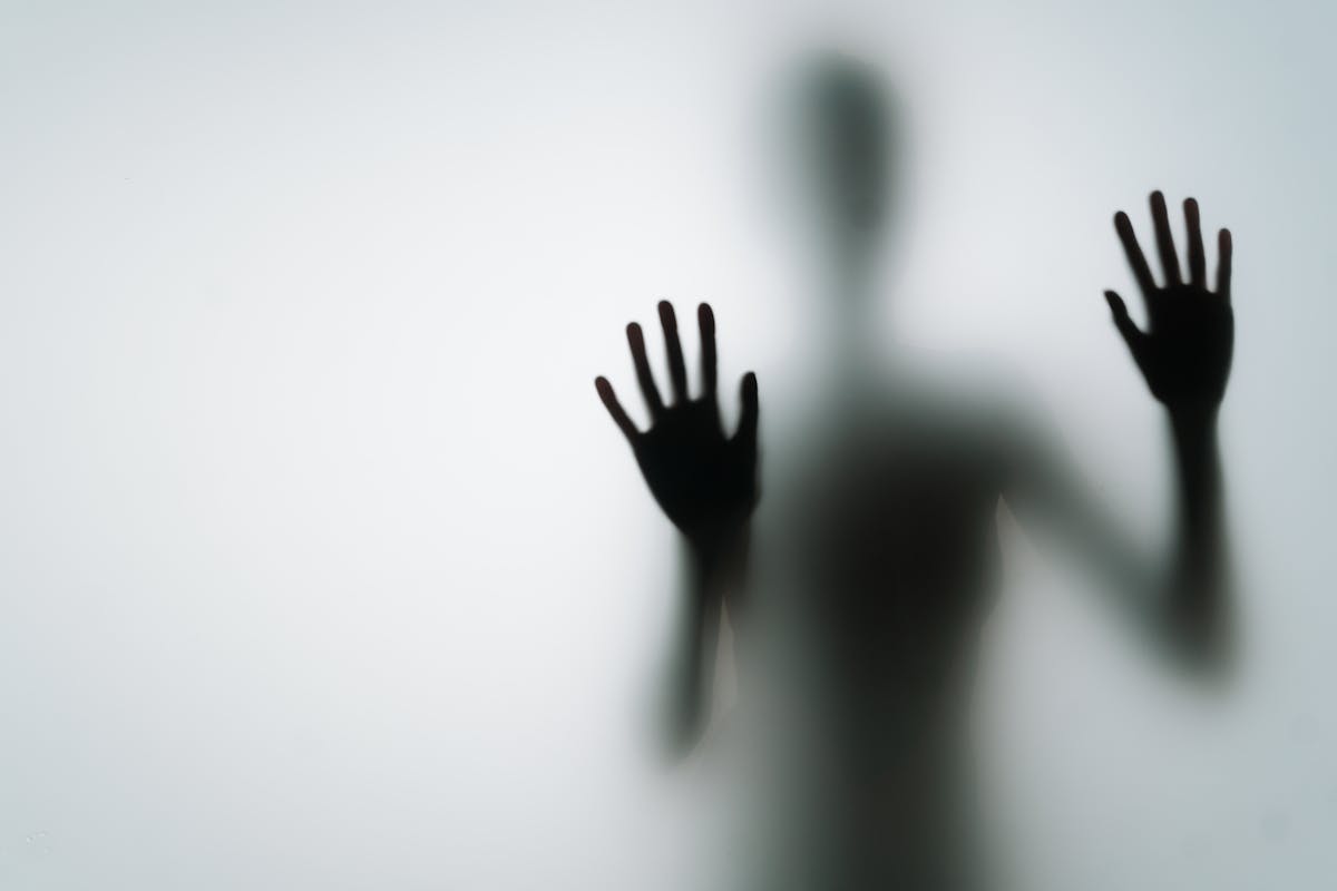Abstract silhouette of a person pressing hands against glass in dim light representing the disturbing experience of finding no reflection at all in a mirror dream