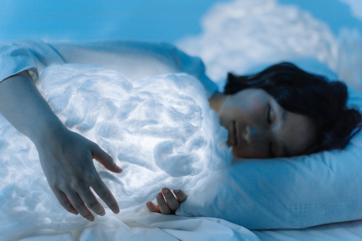 Peaceful image of a woman sleeping on a white pillow with soft blue light suggesting the practice of journaling and working with mirror dreams after waking
