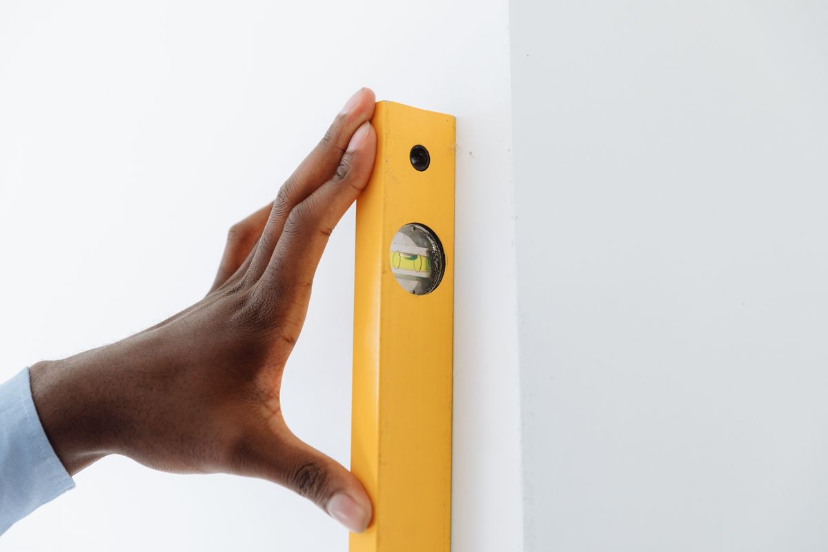 Using a spirit level on a wall to hang a bedroom mirror straight and secure Hand using a spirit level against a wall to hang a mirror straight and at the right height