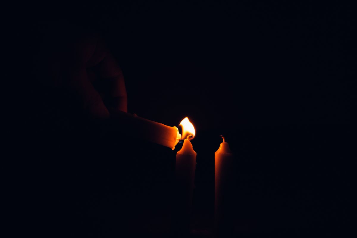 A hand lighting candles in a dark room representing the low-light conditions that induce the alpha-wave state used in black mirror scrying