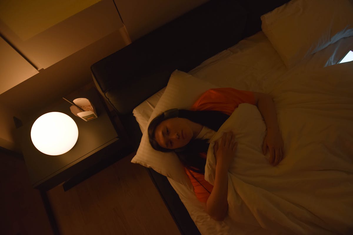 An Asian woman lies awake in bed under dim lighting at night, evoking the folk tradition of mirror dreams as significant spiritual omens