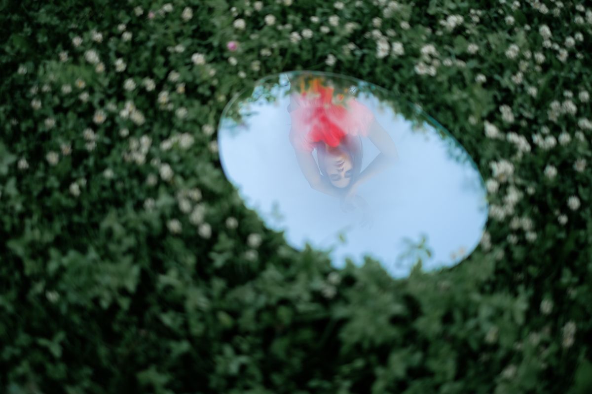 Woman reflected in round garden mirror among greenery showing intentional artistic doubled reflection