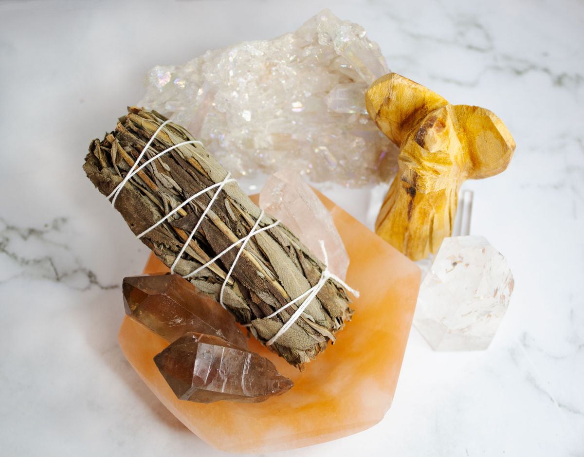 A still life of healing crystals and a sage smudge stick on a marble surface representing the grounding tools used after exploring the broken mirror spiritual meaning