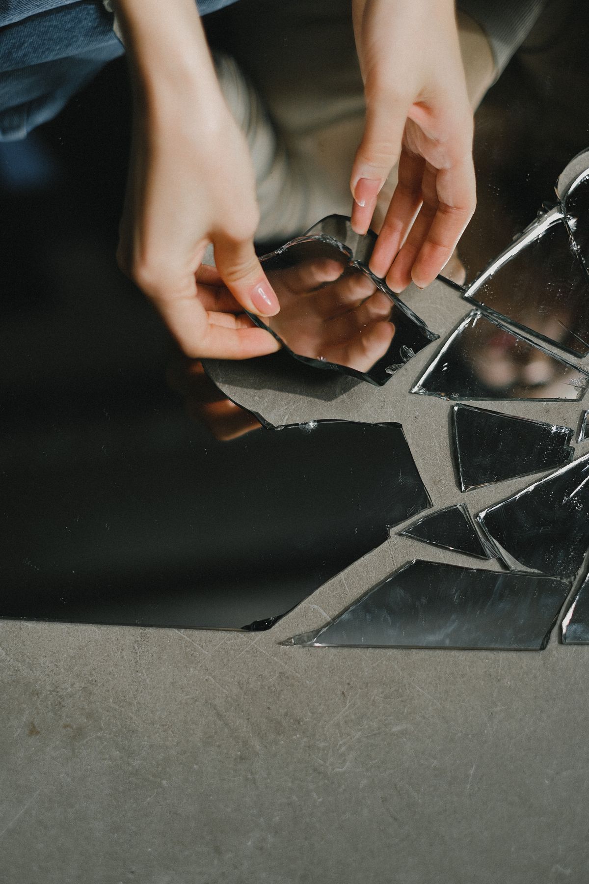 Hands among mirror shards on floor symbolising spiritual introspection after broken mirror dreams Hands touching reflective mirror shards on the floor symbolising introspection after a broken mirror dream