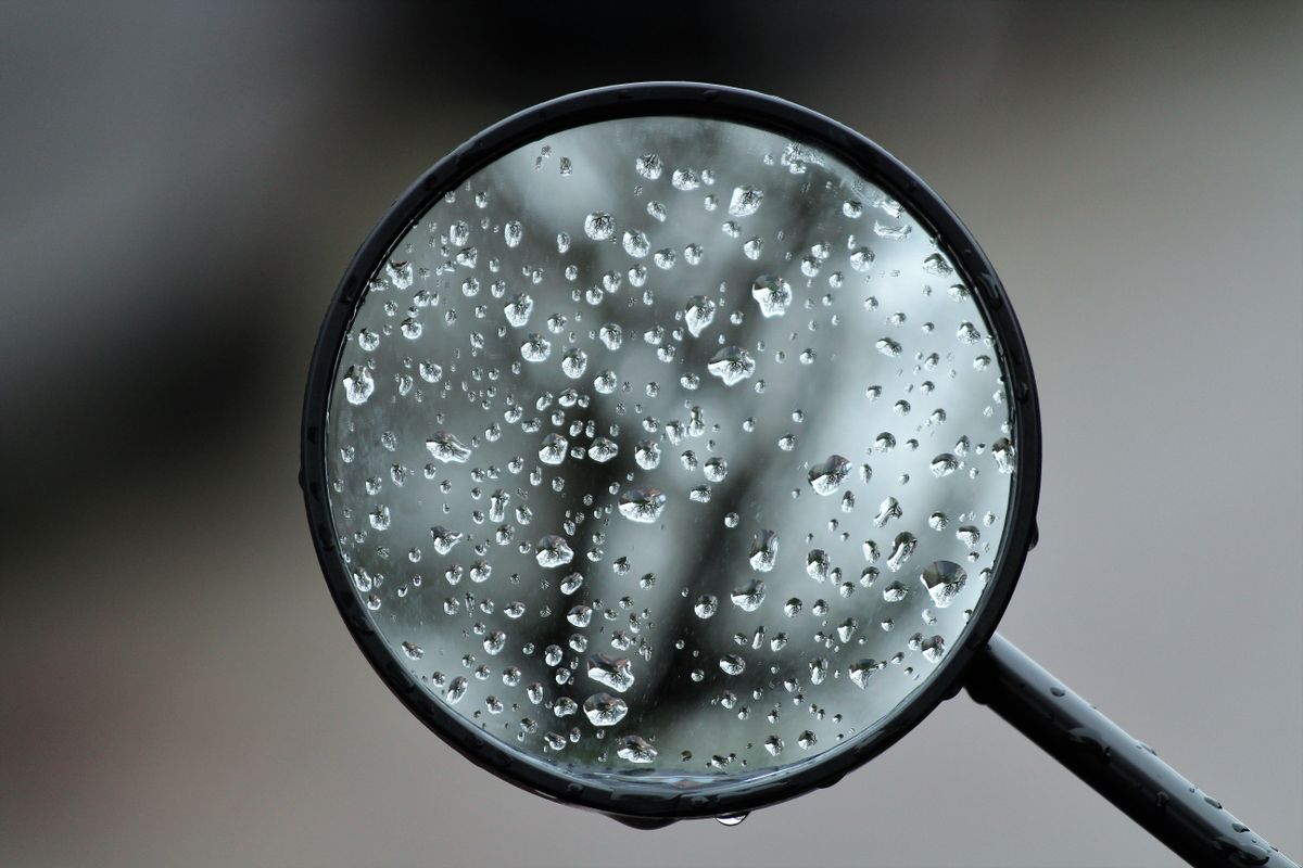 Close-up of dewdrops on a round rearview mirror surface showing the precision reflective coating and how even nanometre-level surface variations affect image coherence and reflectance